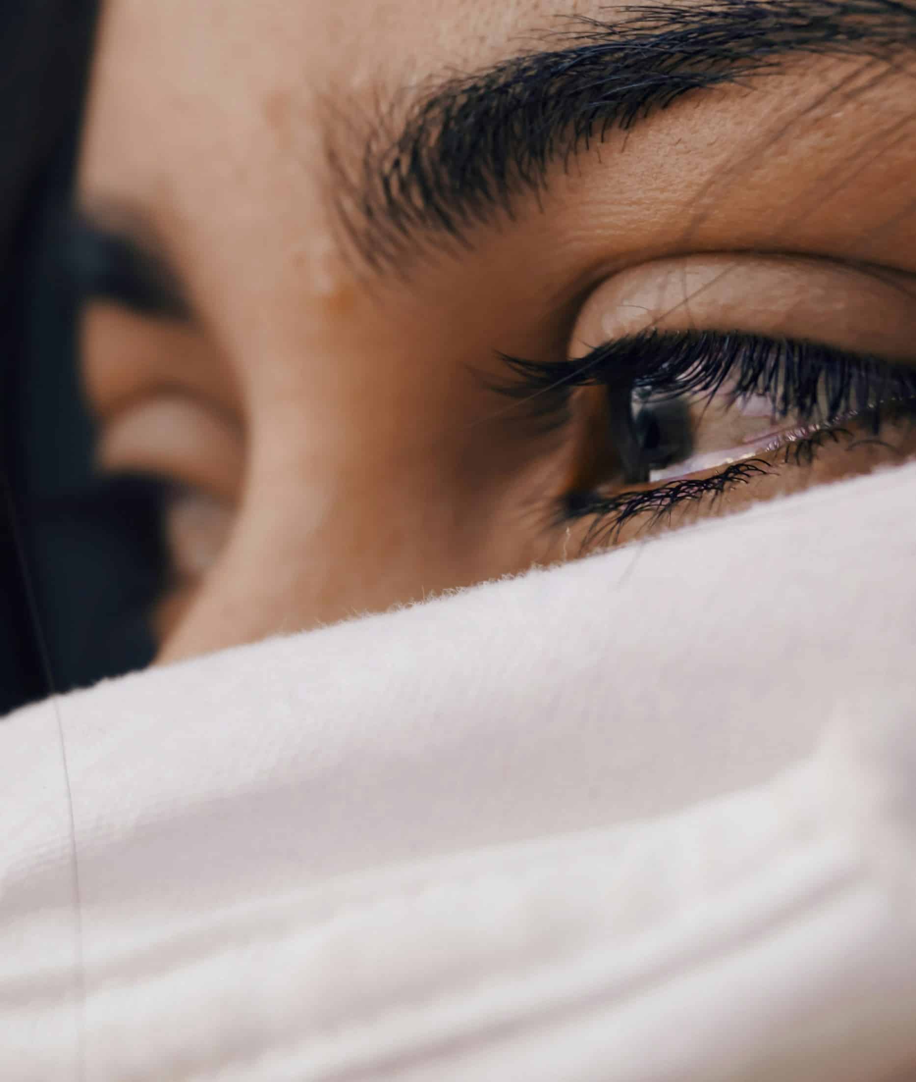 Close-up of a persons eyes, partially covered by white fabric, reminiscent of the introspective aura one might find in psychotherapy. The eyes look away, framed by visible eyelashes and eyebrows, while the fabric hints at mystery or contemplation akin to a session in Godalming.